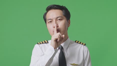 close up of asian man pilot looking at camera and making shh gesture in the green screen background studio