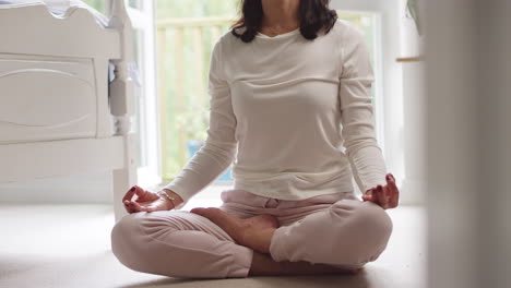 Primer-Plano-De-Una-Mujer-Asiática-Madura-En-Pijama-Sentada-En-El-Suelo-Del-Dormitorio-Meditando-En-Pose-De-Yoga---Filmada-En-Cámara-Lenta