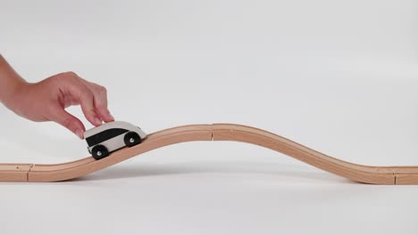 hand moves toy car on wavy wooden track