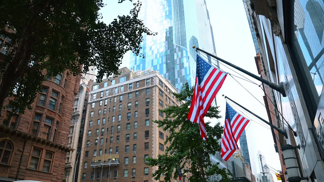 New York, USA, 28 agosto 2025: due bandiere americane sui pennoni delle facciate degli edifici. Vista dal basso dei grattacieli di New York e degli alberi che vi crescono