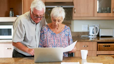 senior couple calculating their bills on laptop in the kitchen