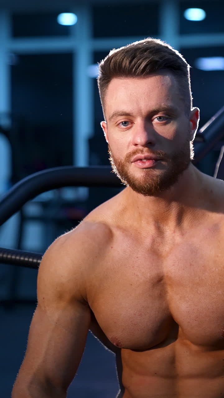 Shirtless bodybuilder at fitness gym. Handsome man with muscles posing at the camera in the gym. Vertical video