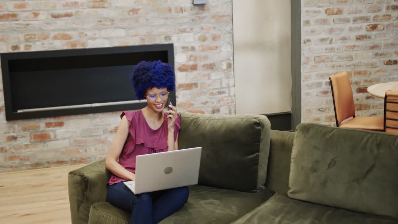 Biracial businesswoman talking on smartphone and using laptop in office, copy space, slow motion