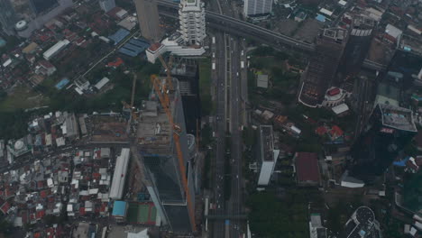 Aerial-tilting-dolly-shot-of-tall-skyscraper-under-construction-revealing-city-skyline-in-the-background