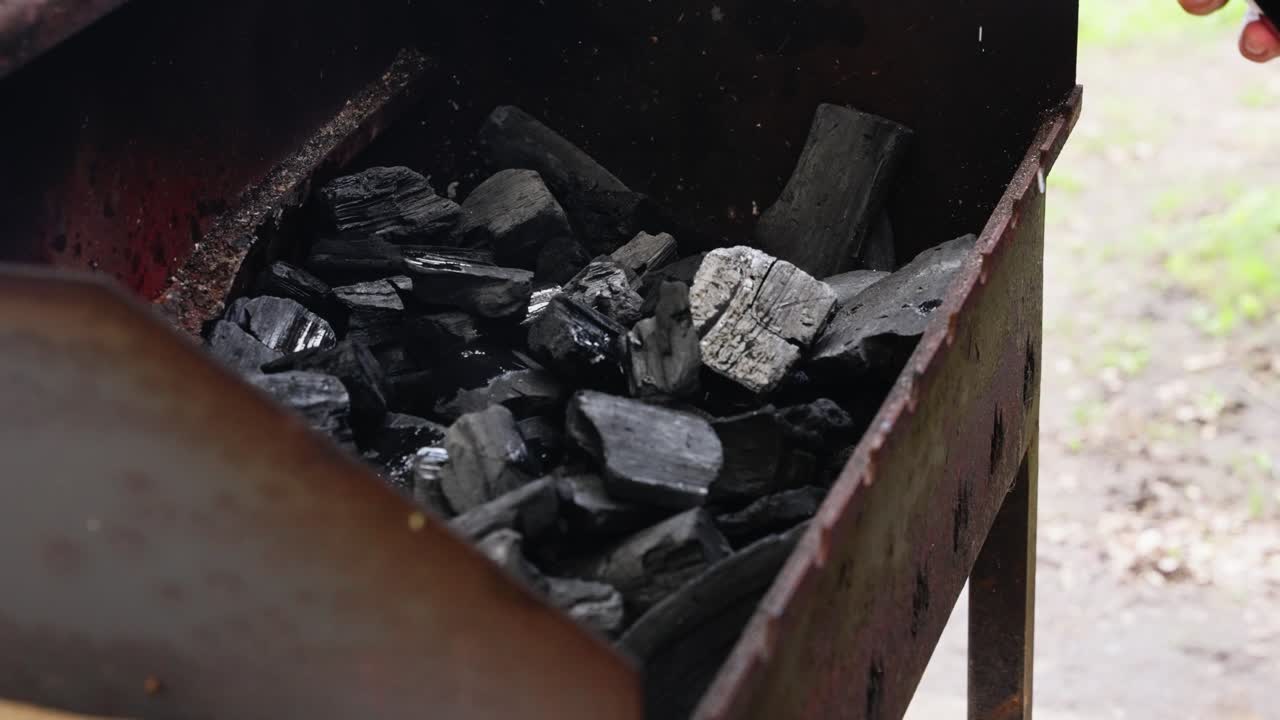 Liquid splashes over black charcoal as grill prep begins in outdoor setting