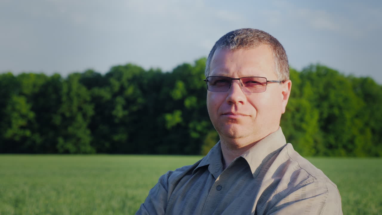 Portrait Of A Successful Farmer Looking At The Camera Against The Background Of A Green Wheat Field 