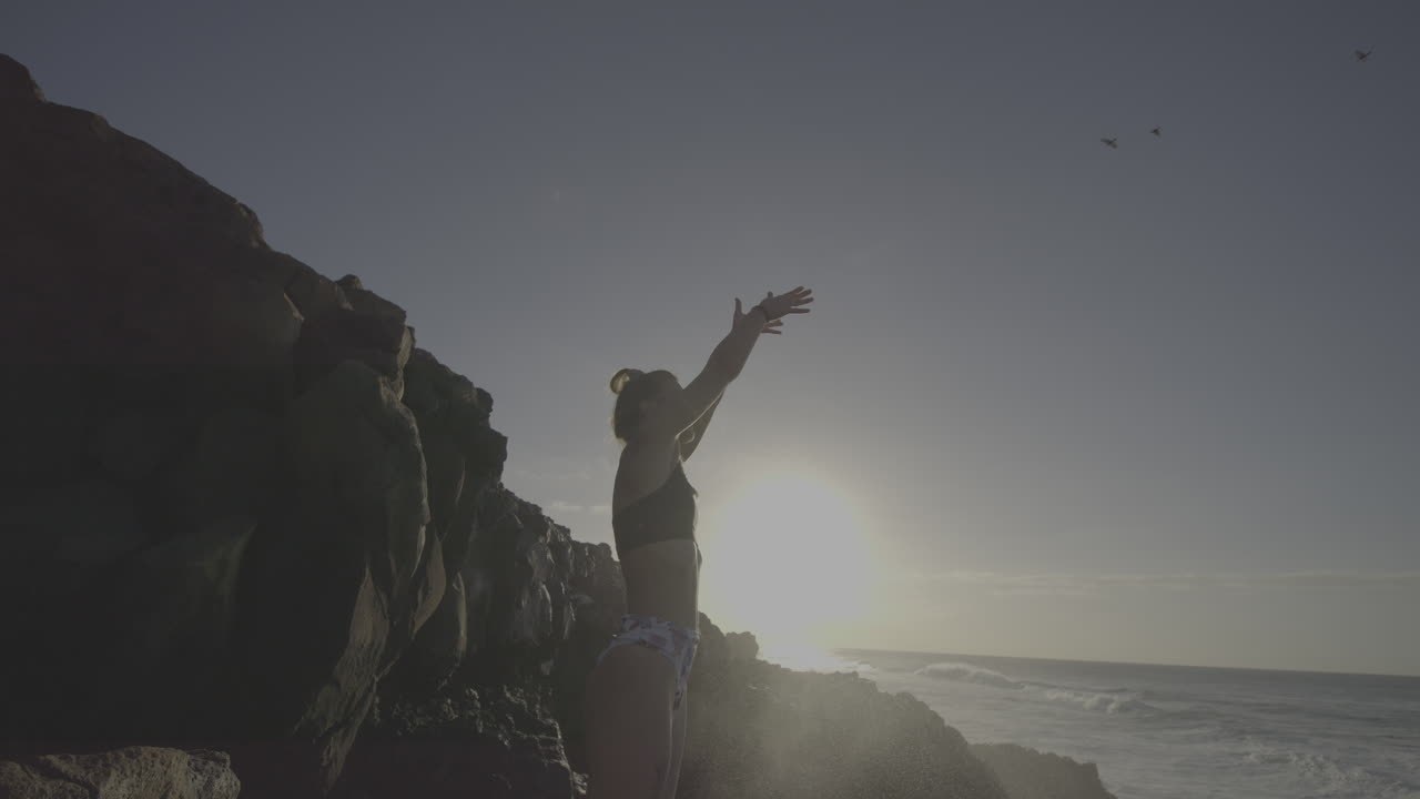 Woman practicing yoga by the ocean at sunrise/sunset