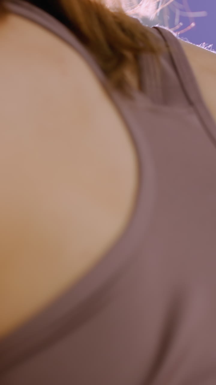 близкий боковой вид молодой женщины, слегка согнутой в коричневой спортивной одежде, тянущей тяжести в тренажерном зале, сосредоточенной на силовой тренировке с легким отражением с правой стороны