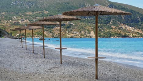 Sonnenschirme-Aus-Holz-Am-Strand-Von-Agia-Kiriaki-An-Den-Klaren,-Blauen-Wellen---Breit