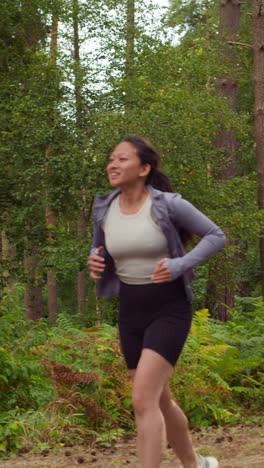 Toma-De-Video-Vertical-De-Una-Pareja-Haciendo-Ejercicio-Al-Aire-Libre-Corriendo-Por-El-Bosque-Con-Un-Hombre-Animando-A-Una-Mujer-Cansada-Que-Viste-Ropa-Deportiva,-Filmada-En-Tiempo-Real