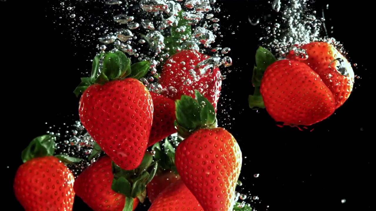 Fragole rosse fresche che cadono nell'acqua con bolle su sfondo nero