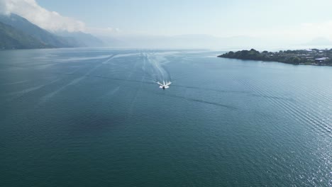 drone view in guatemala flying over a boat on a blue lake with green mountains on the side on a sunny day in atitlan