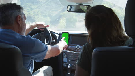Senior Hispanic Couple On Drive Through Countryside Using Sat Nav On Mobile Phone