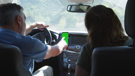 senior hispanic couple on drive through countryside using sat nav on mobile phone