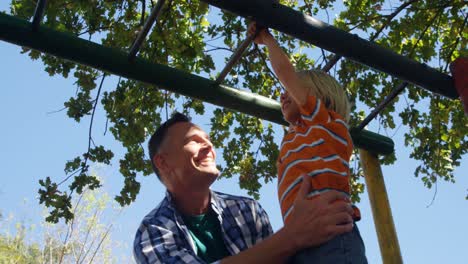 padre ayudando a su hijo a escalar barras de mono en el patio de recreo 4k