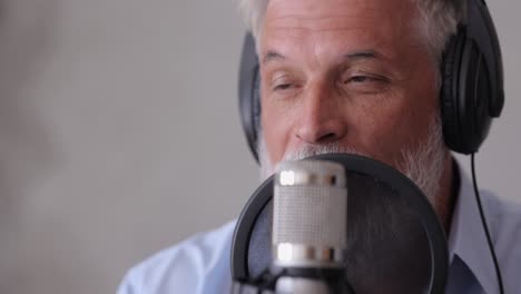 man records a podcast or interview with a microphone in a recording studio. senior sound engineer or radio host. an adult gray-haired man creates audio content