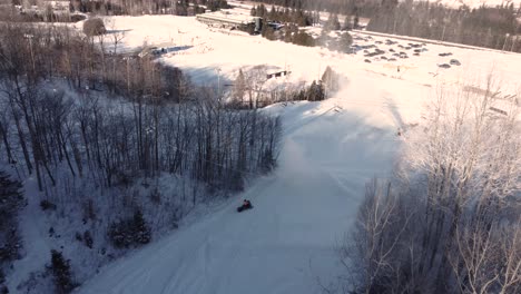 Tracking drone shot of snowmobile going down on the ski slope while snow gun blowing snow in Saint-Sauveur, Quebec, Canada