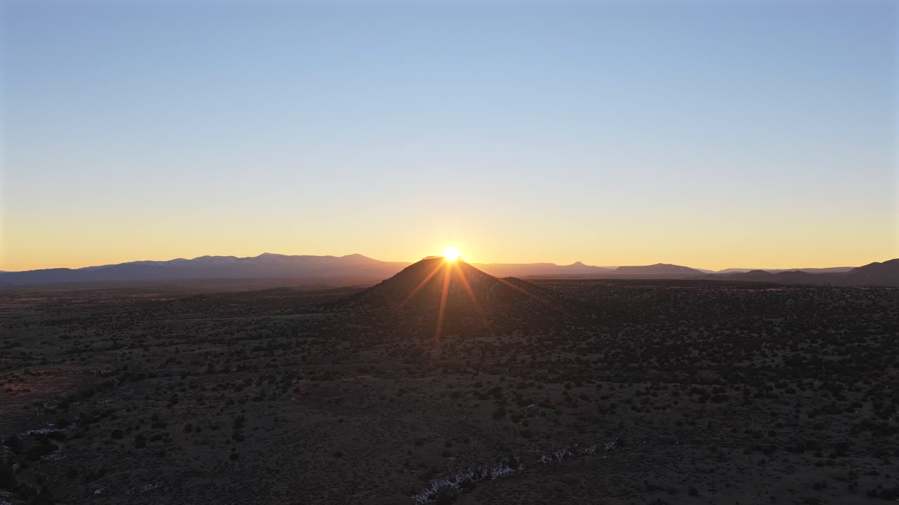 A dramatic drone flight pushes toward a lone desert mesa as the sun breaks over the peak. This 4K shot captures a brilliant golden hour starburst across a vast Southwest landscape
