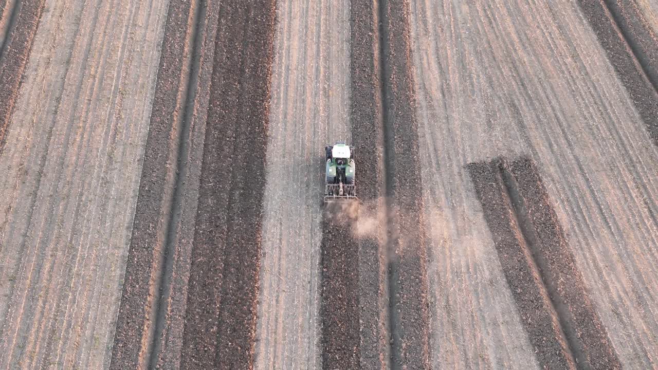 Aerial drone image of a tractor tilling soil in parallel rows during late autumn in the Po Valley, Northern Italy. Dust trails highlight active mechanized farming under clear morning light