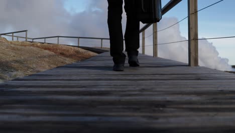 Adventure-photographer-with-camera-case-walking-on-wooden-path-at-geothermal-geysers,-Iceland