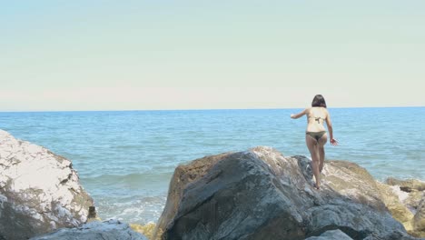 young attractive woman in two piece bikini climbing over rocks near the beach