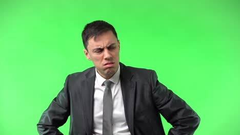 a man in a suit on a green screen displaying various expressions of pain, confusion, and discomfort