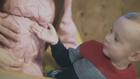 Un-Niño-Gracioso-Mira-A-Una-Mujer-Embarazada-Con-Un-Jersey-Rosa-En-El-Vientre