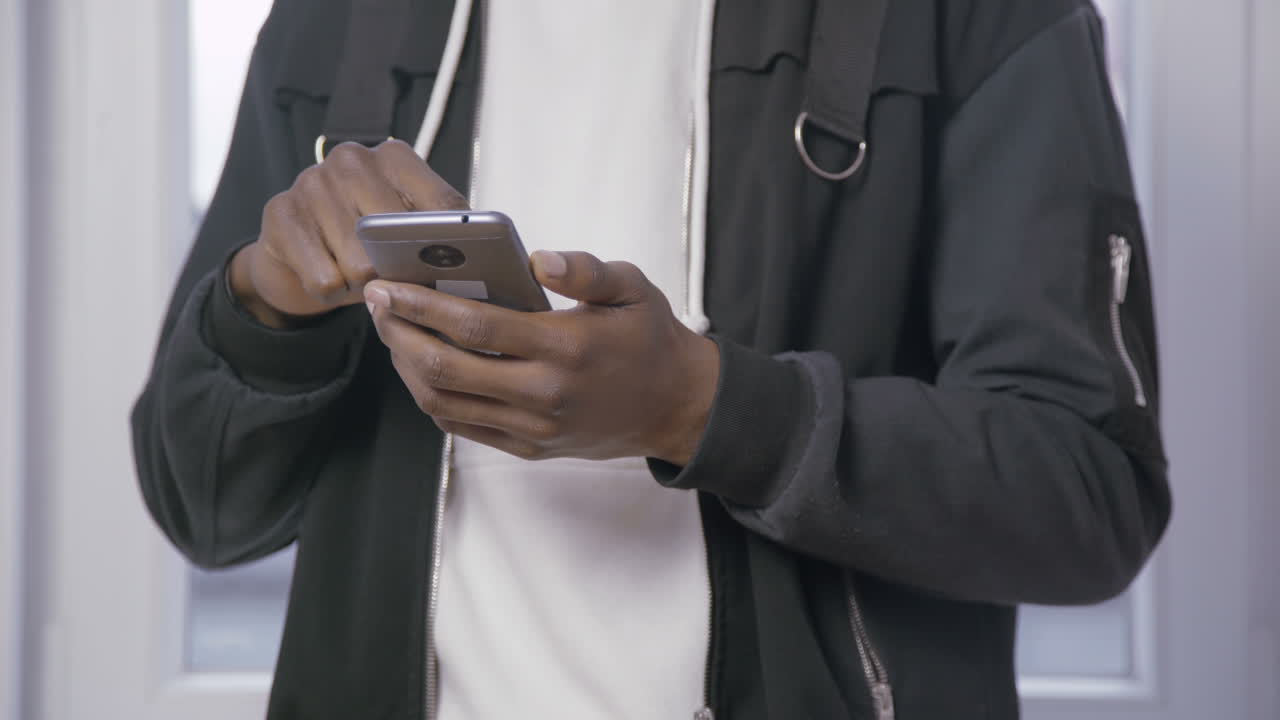 Mani di un uomo afroamericano che digita un messaggio su smartphone.