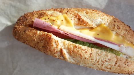 a close-up of a delicious sandwich with ham, cheese, lettuce, and tomato on a sesame seed bun