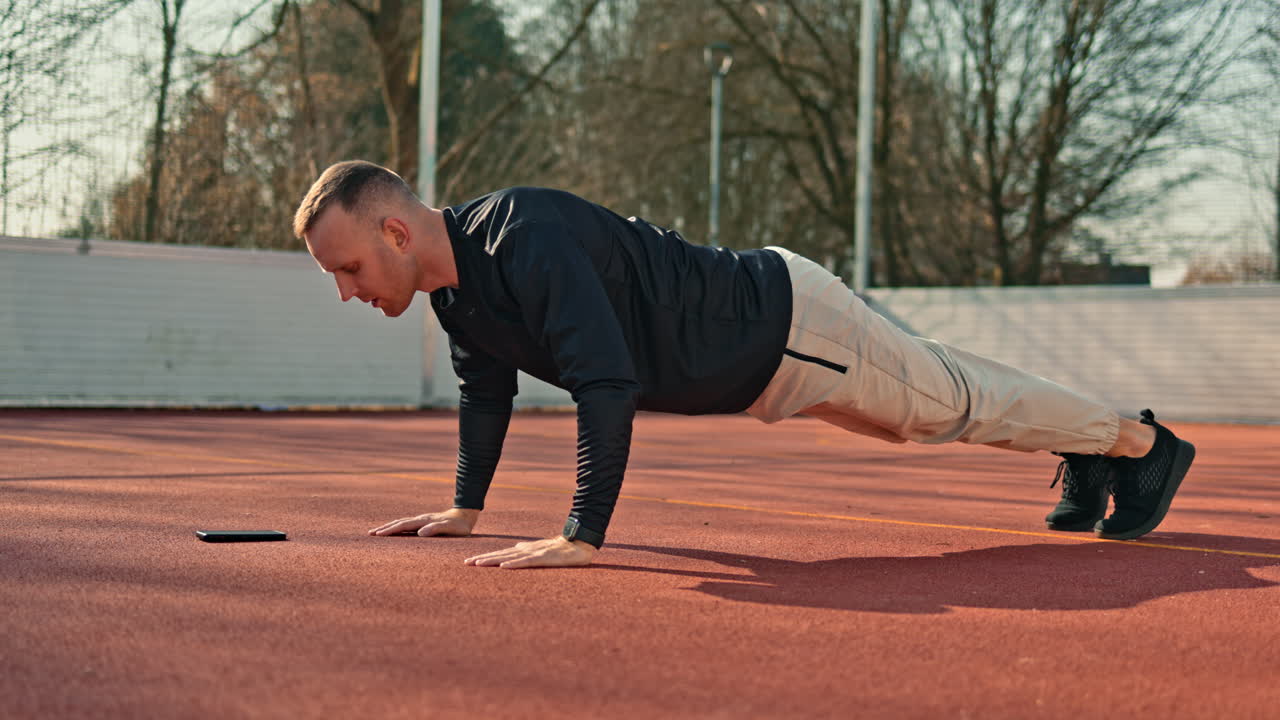 Un giovane in tuta da ginnastica e maglia sportiva fa sport su un campo da basket. Un uomo dal corpo atletico si allena all'aperto.