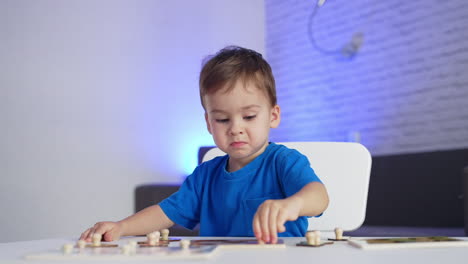 adorable little toddler in blue t-shirt playing peacefully at the desk. baby boy matching puzzle pieces. blurred backdrop.