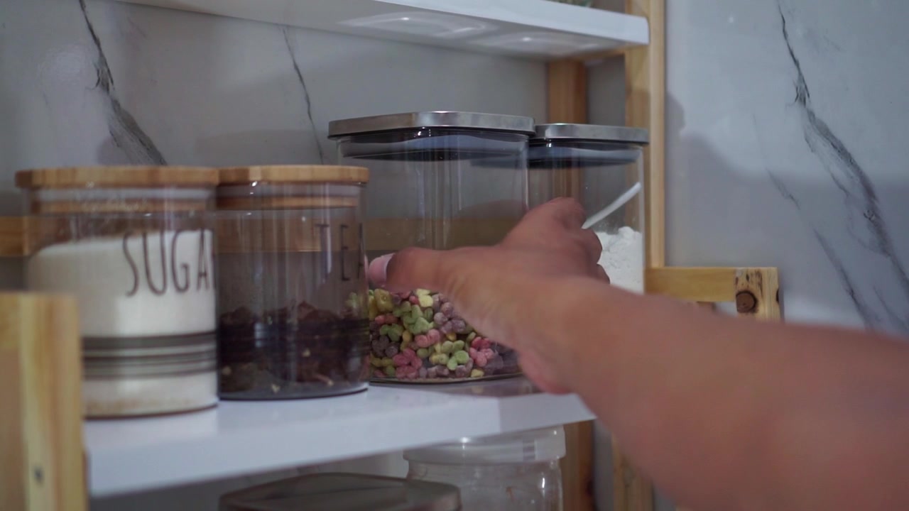 Persona che prende un contenitore colorato di cereali dallo scaffale, barattoli di vetro con coperchi, concetto di organizzazione della cucina