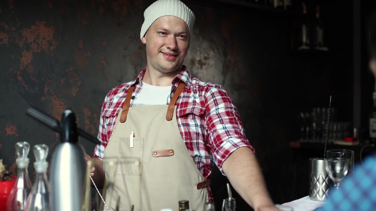 Venlig bartender rører en cocktail og smiler til en kunde