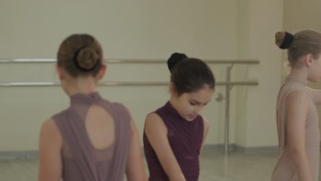 a group of young ballet students in black dancewear practicing positions in a spacious ballet studio with wooden flooring and wall-mounted barres. focused expressions and synchronized movements.