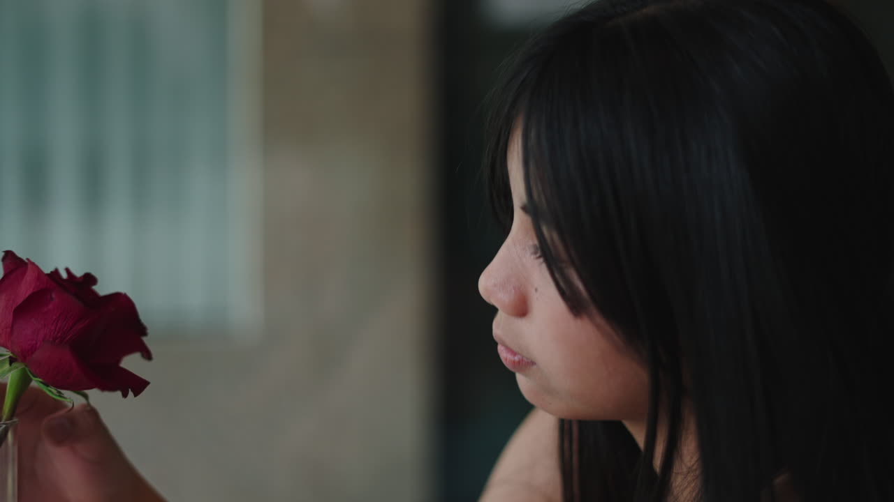 赤いバラの香りを嗅いで息を吹きかける若いアジア人女性