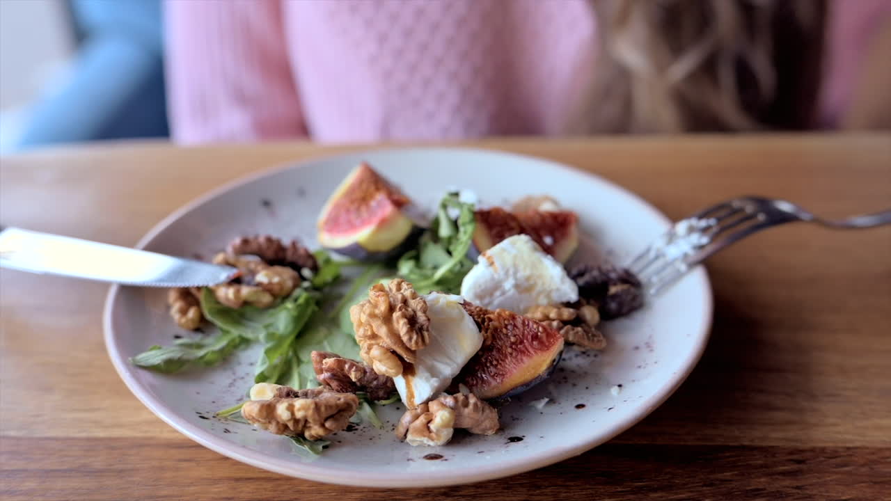 Woman eating a fig salad with nuts and cheese at a restaurant