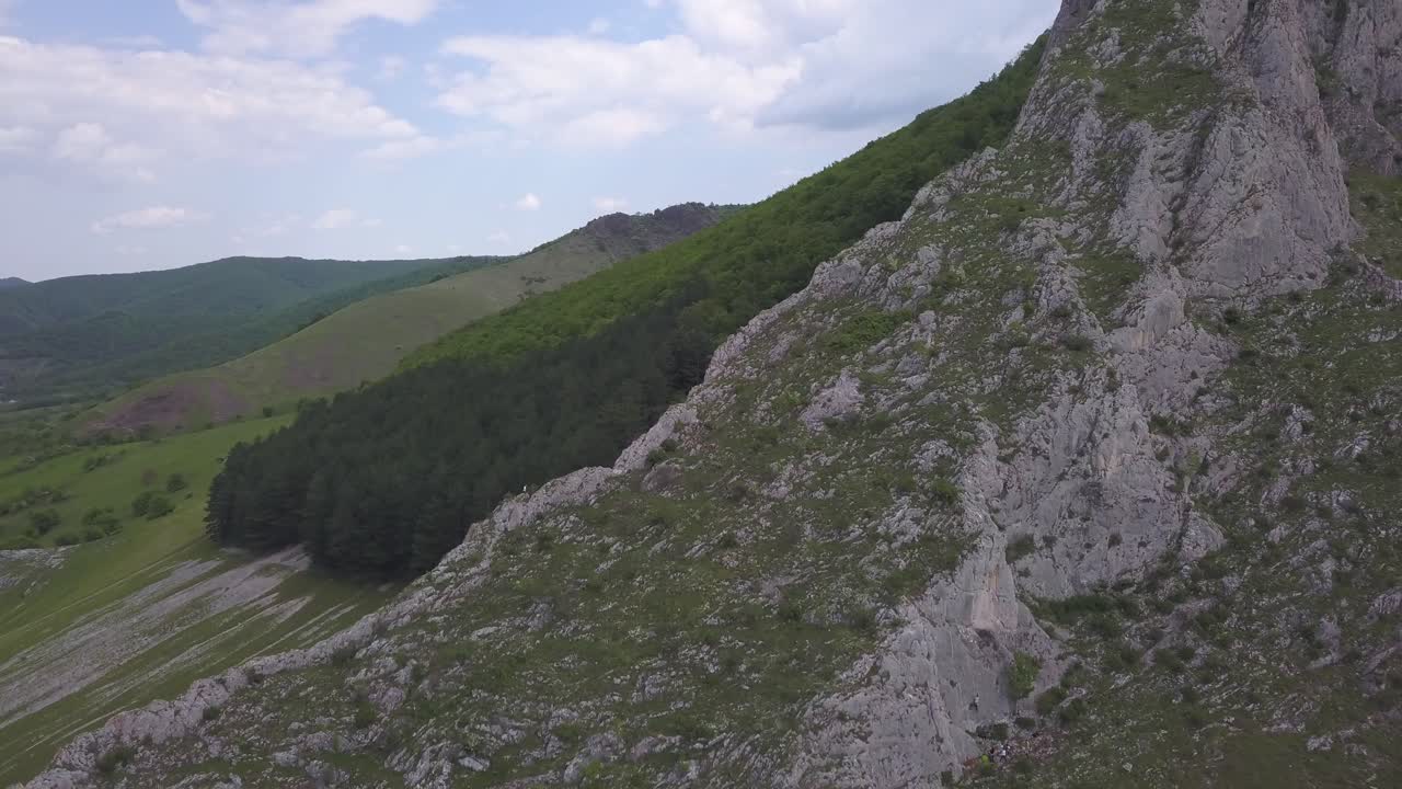 Aerial View Of Hiker Climbing Up a Rock Mountain In Nature With Green Vegetation In Horizon