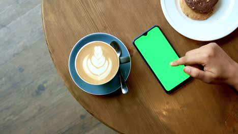 hand using smart phone with green screen on cafe table