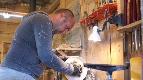 carpenter in sawdust inspects product at lathe.