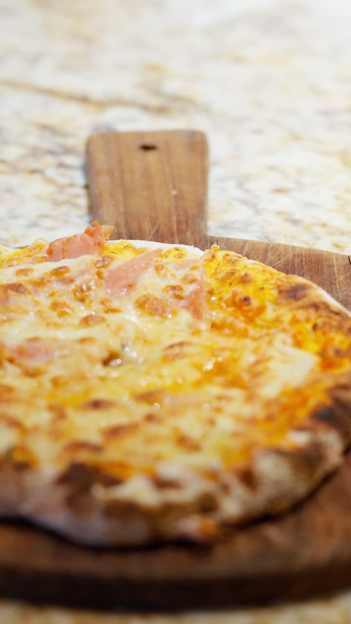 Slow motion vertical pan across a fresh hot pizza with melted cheese and a crispy crust served on a wooden board