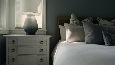 Dimly-lit-bedroom-with-nightstand,-lamp,-and-sunlit-bed