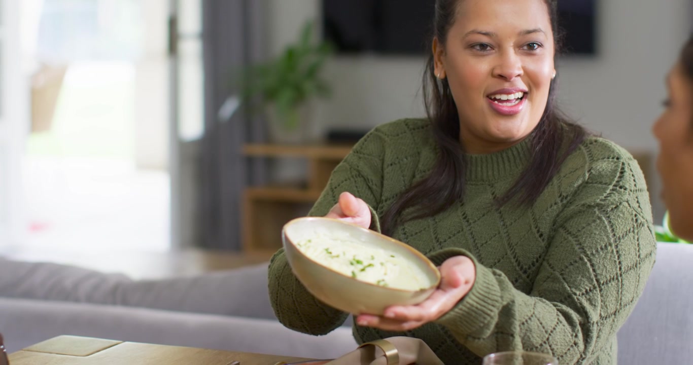 African American pair at home, woman in green sweater sharing soup guest holding glass, copy space
