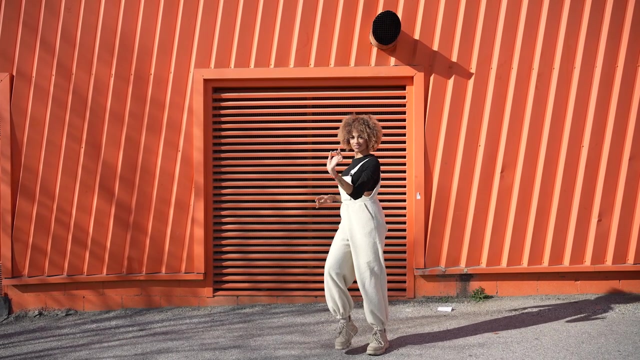 A modern dancer is posing gracefully against a bright and vibrant orange wall background