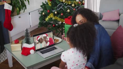 Happy-african-american-mother-and-daughter-on-video-call-on-laptop-with-grandparents-at-christmas