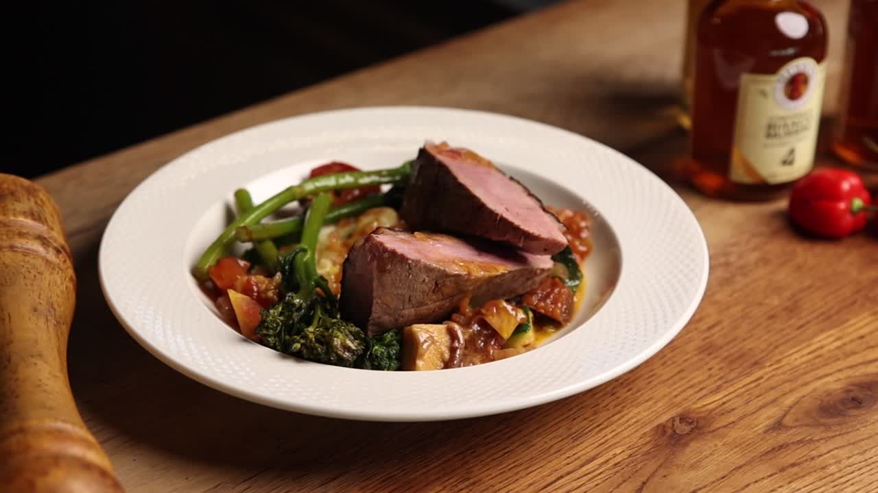 Piatto gourmet di carne cotta con verdure fresche su un tavolo di legno.