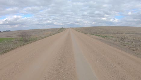 point of view driving on a straight stretch of gravel road, slowing to make a turn onto a cross road