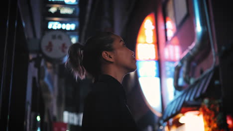 Woman-dressed-in-black-looks-up-contemplatively-in-a-vibrant-urban-night-scene