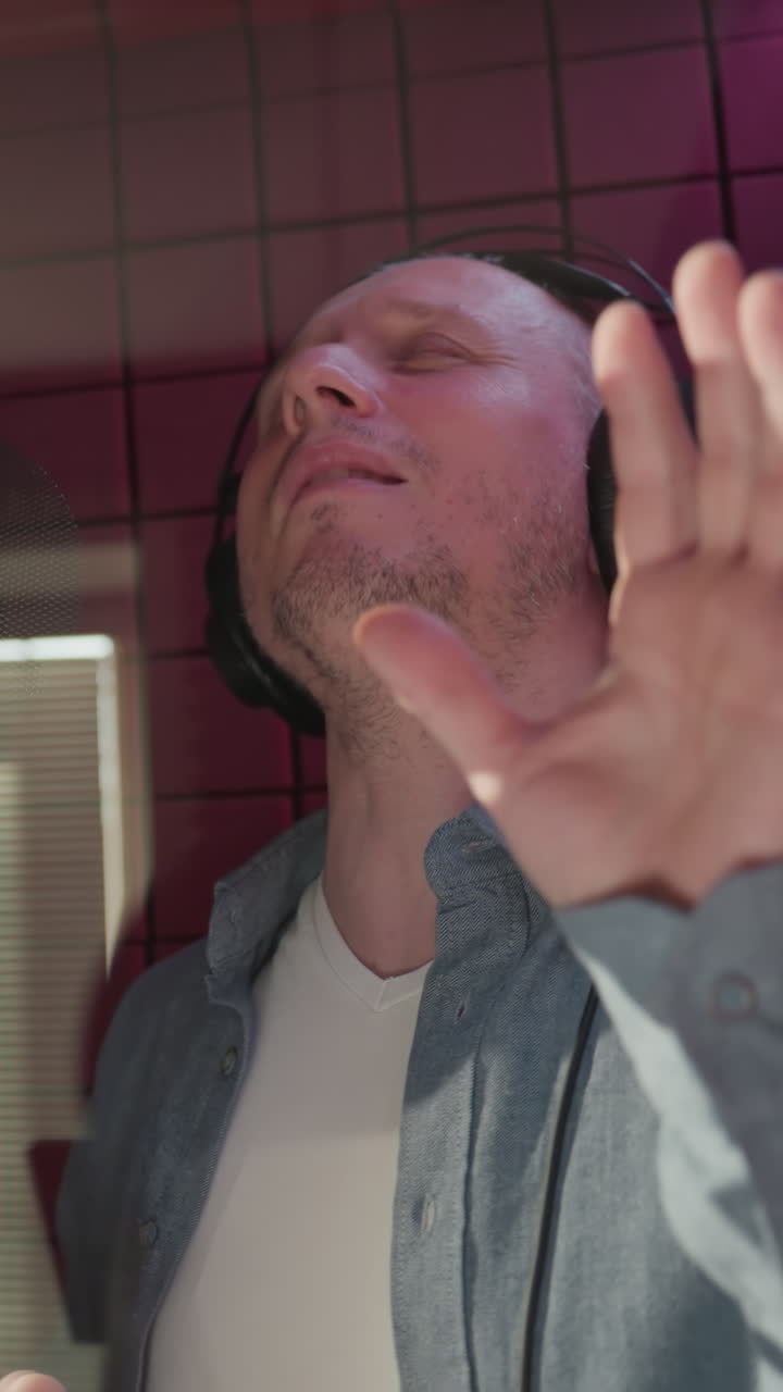 primer plano de dos hombres en una habitación a prueba de sonido roja, cantando apasionadamente, completamente inmersos en la música. uno lleva una gorra y camisa negra, mientras que el otro está vestido con una camisa azul y una camisa interior blanca