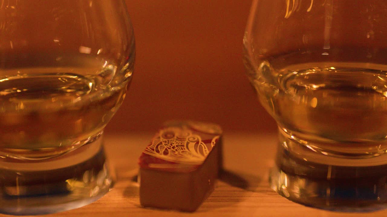 Close-up of whisky glass and chocolate, slow camera pan, warm ambient lighting, inviting atmosphere