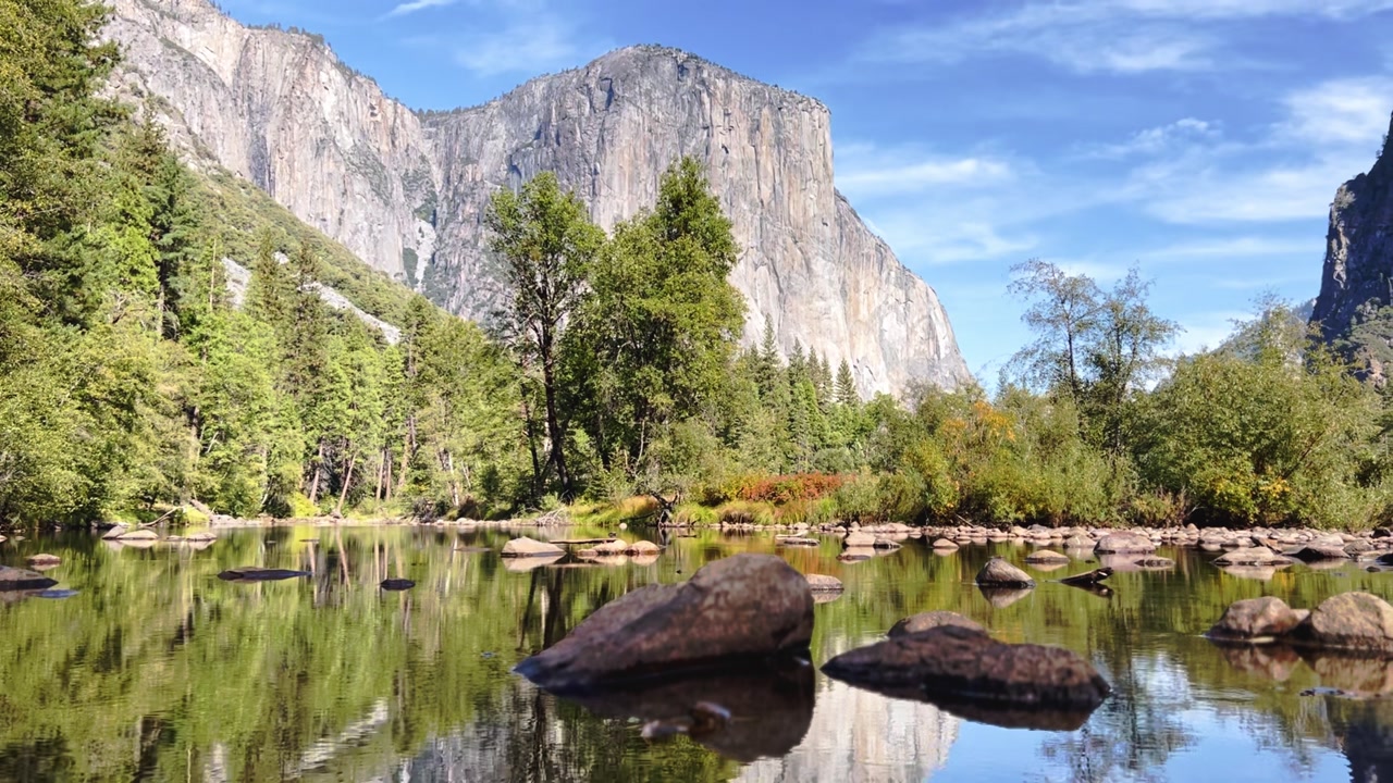 El Capitan reflects clearly in still water with surrounding forest and rocks in Yosemite Valley.
